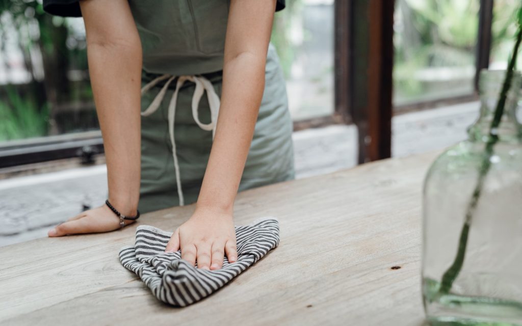 seseorang sedang membersihkan meja kayu dengan kain lap